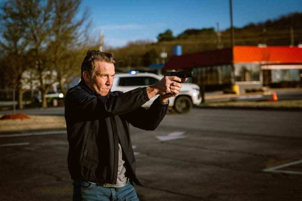 Dennis Quaid aiming a gun to the right.